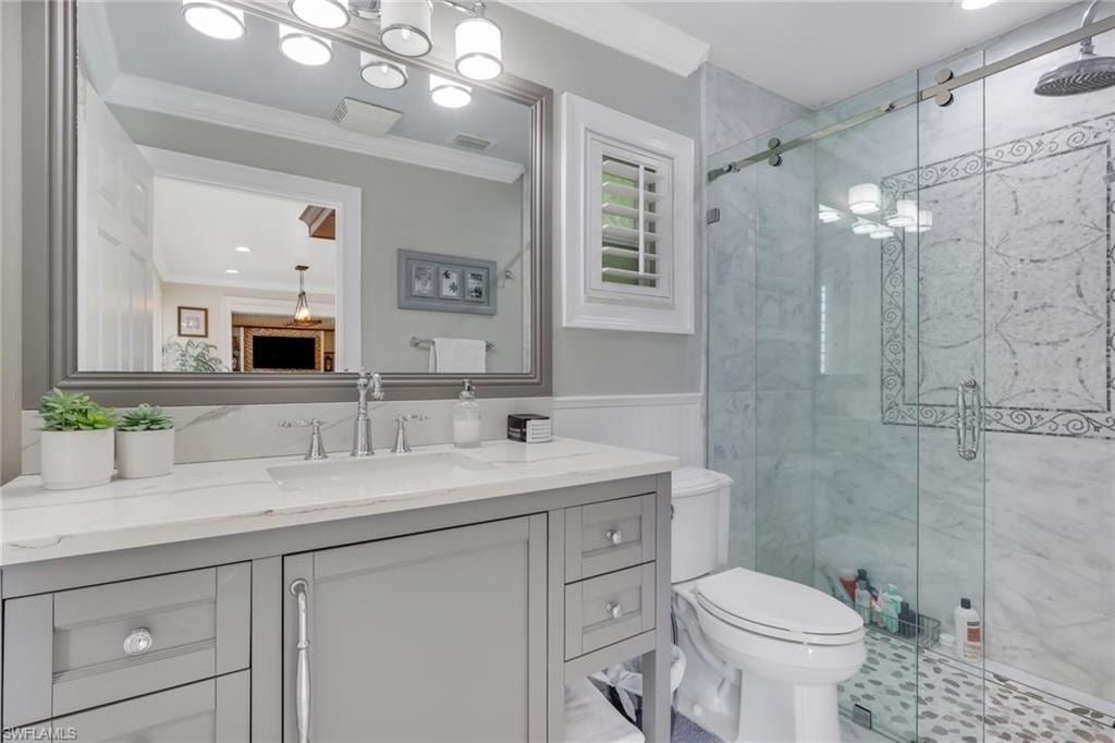 Bathroom with ornamental molding, vanity, a marble finish shower, recessed lighting, and wainscoting