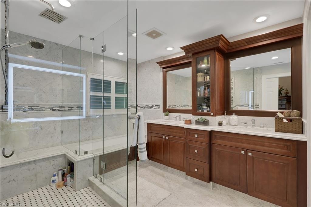 Bathroom with a marble finish shower, double vanity, tile walls, and recessed lighting