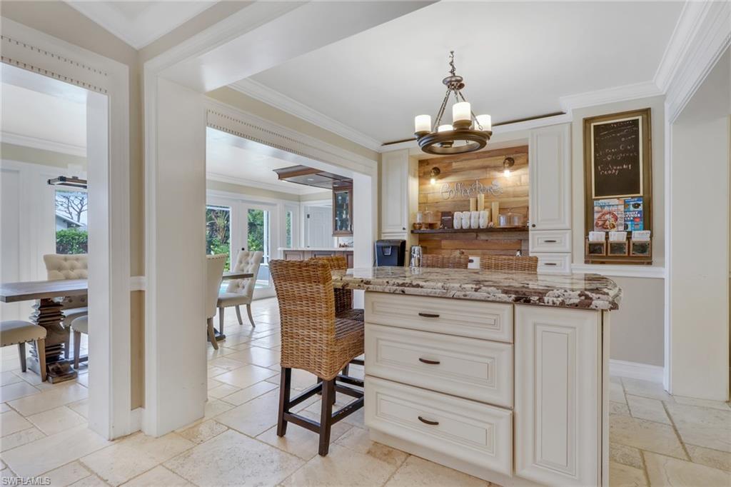 Bar area featuring ornamental molding, light stone countertops, stone tile floors, hanging light fixtures, and white cabinets