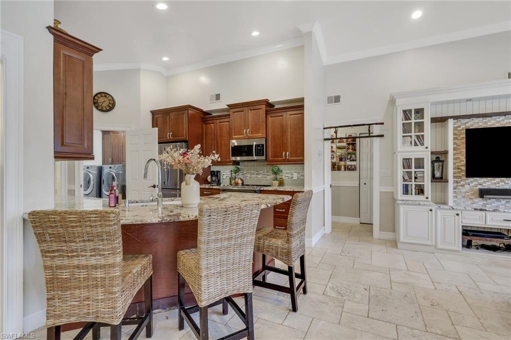 Kitchen with a kitchen bar, light stone countertops, appliances with stainless steel finishes, backsplash, and brown cabinets
