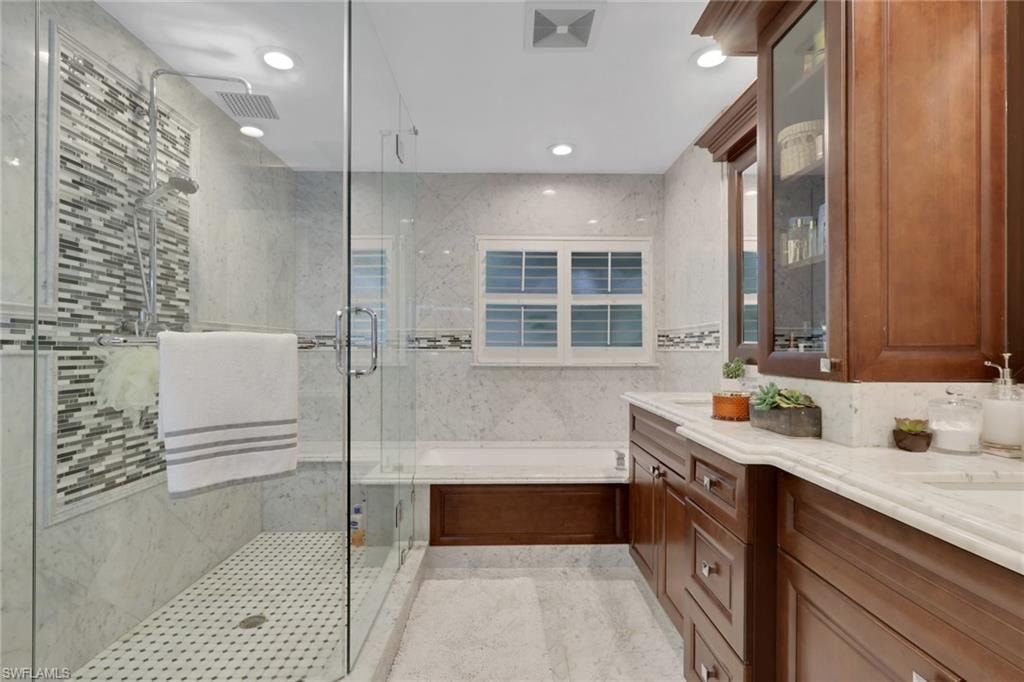 Bathroom with a bath, a shower stall, double vanity, recessed lighting, and tile walls