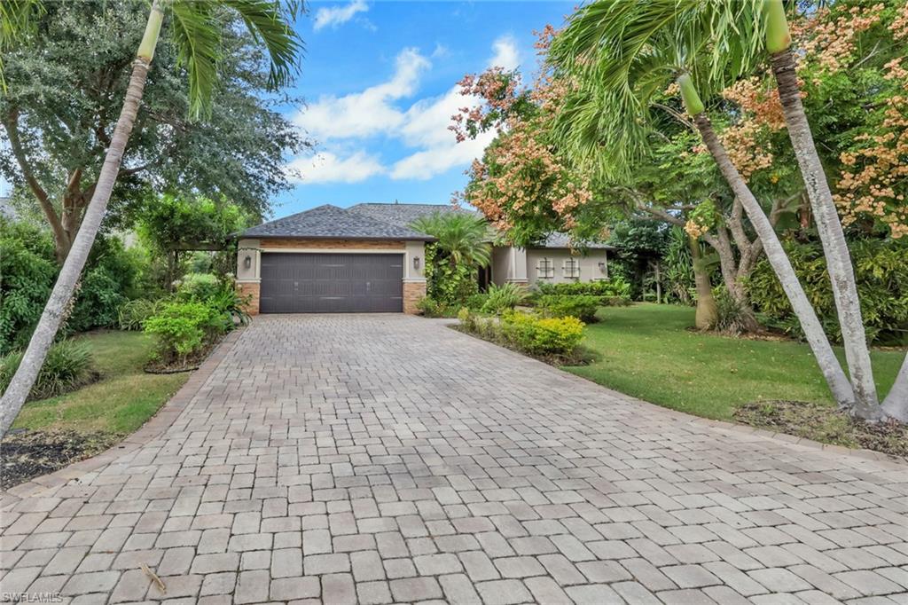 View of front facade featuring stone siding, decorative driveway, an attached garage, and a front lawn