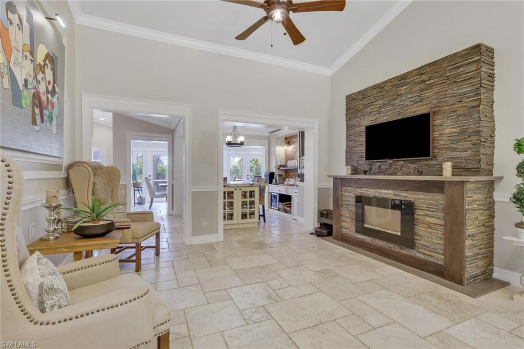 Living area with ornamental molding, stone tile floors, a fireplace, a ceiling fan, and a high ceiling