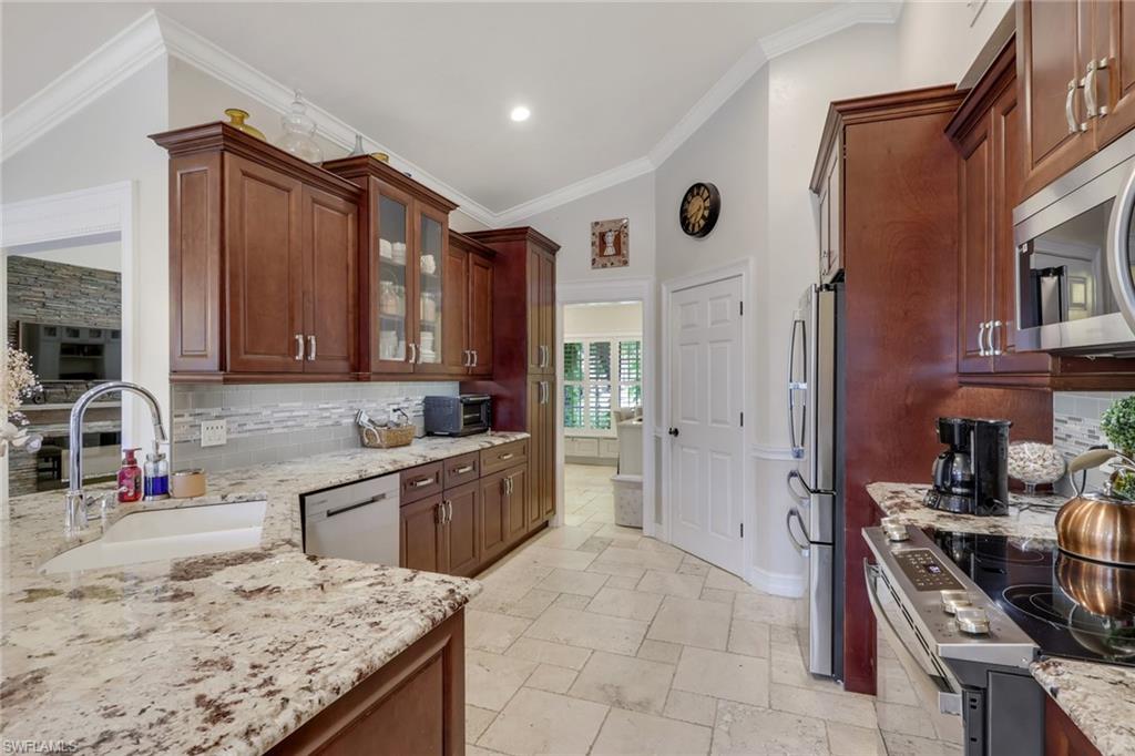 Kitchen with tasteful backsplash, stainless steel appliances, glass insert cabinets, light stone counters, and stone tile flooring