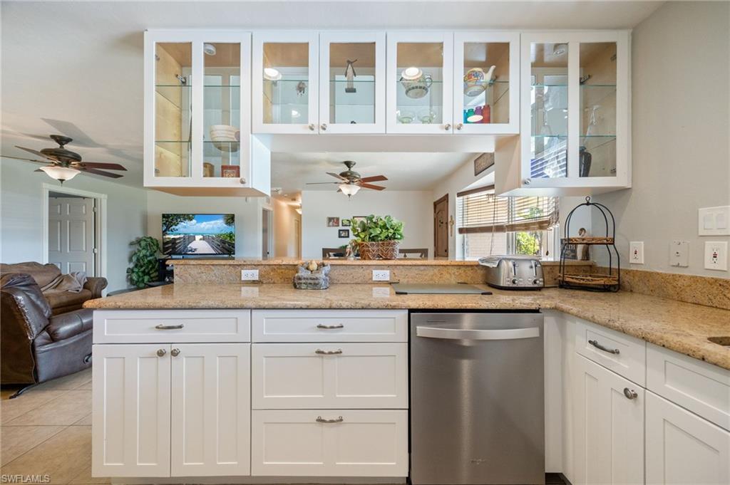 Kitchen with white cabinetry, open floor plan, a peninsula, dishwasher, and light stone counters