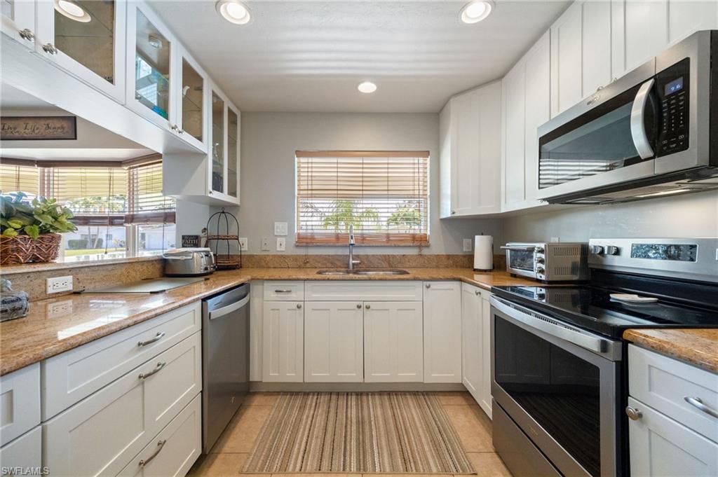 Kitchen with appliances with stainless steel finishes, recessed lighting, white cabinets, glass insert cabinets, and light stone countertops