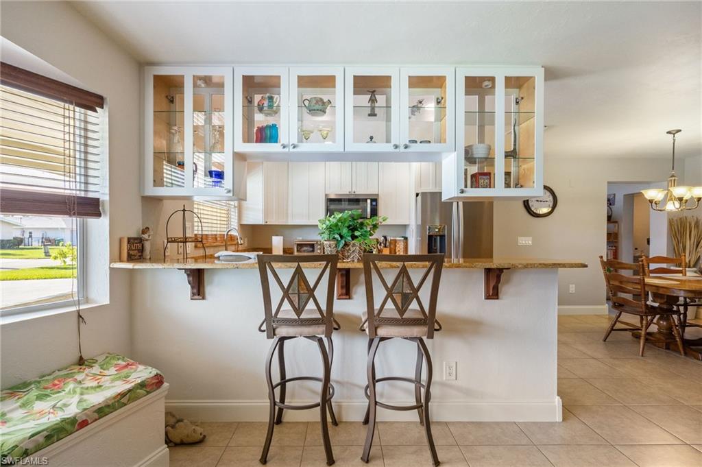 Kitchen with white cabinets, a kitchen breakfast bar, light stone counters, a peninsula, and light tile patterned floors