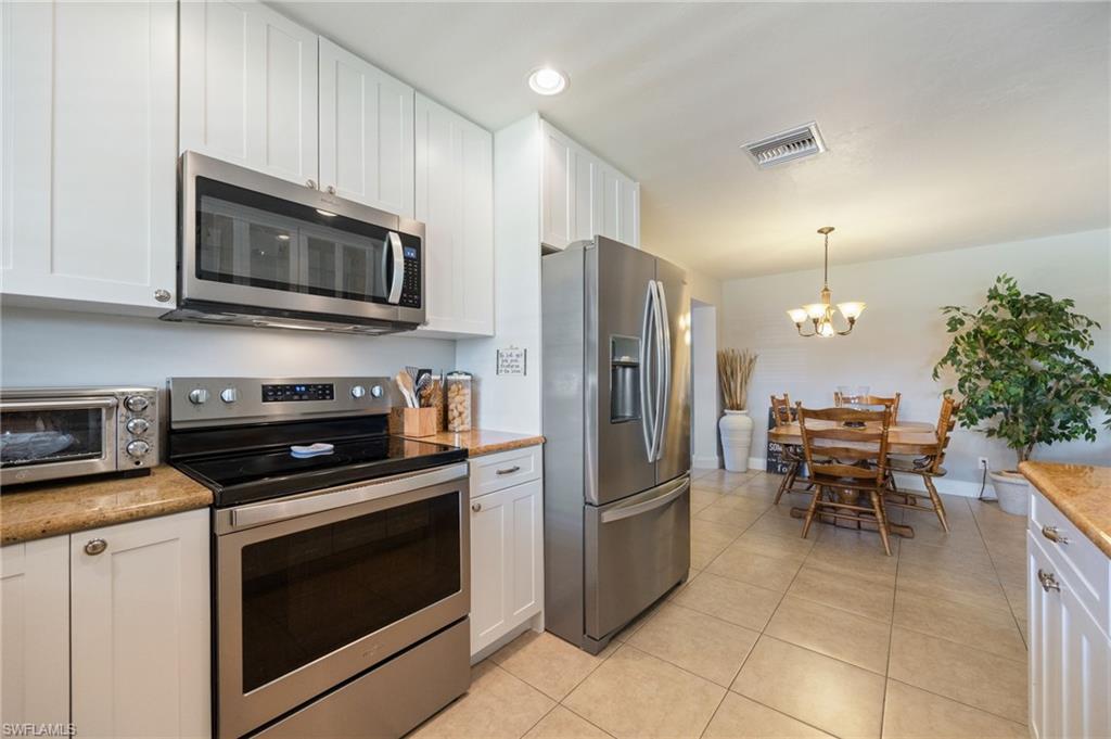 Kitchen with stainless steel appliances, white cabinets, light tile patterned flooring, a chandelier, and decorative light fixtures