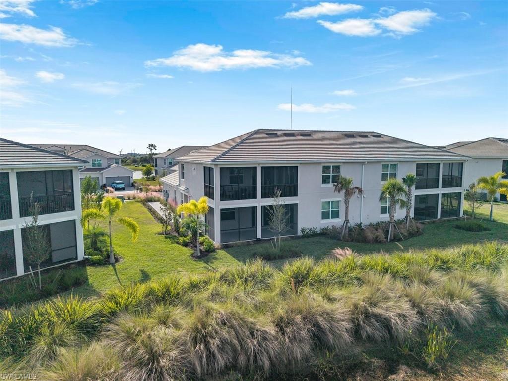 Back of property with a sunroom, a lawn, stucco siding, and a tiled roof