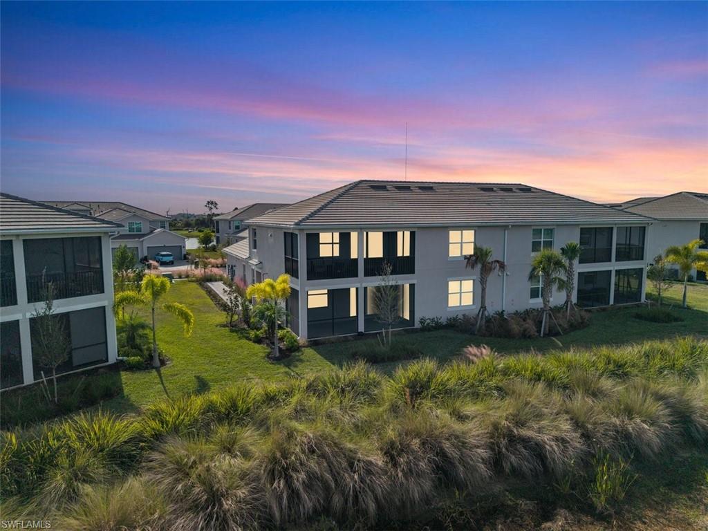 Back of property at dusk with a lawn, a sunroom, and stucco siding