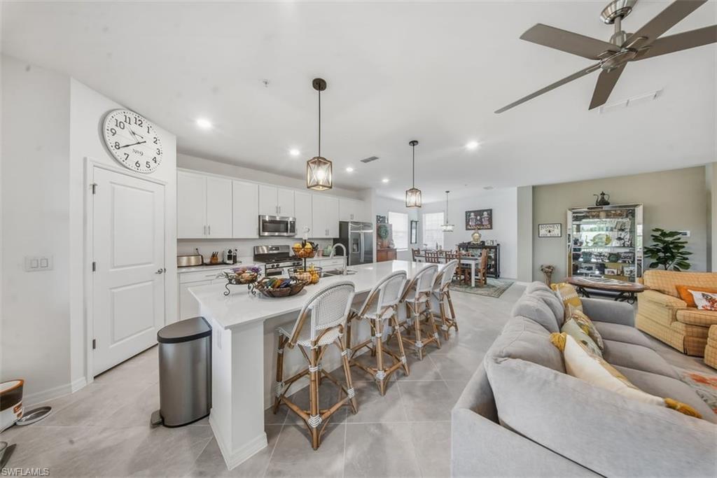 Kitchen with a breakfast bar, an island with sink, open floor plan, pendant lighting, and white cabinets