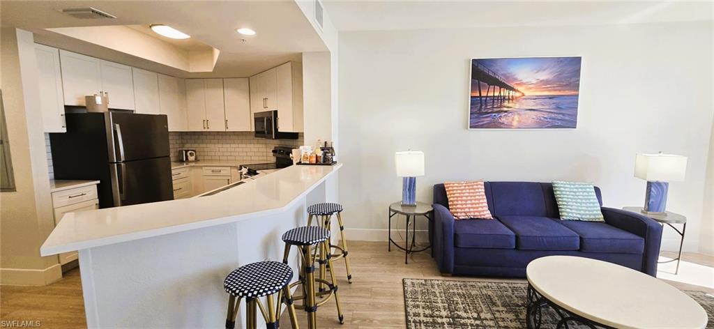 Kitchen featuring backsplash, light wood-style floors, appliances with stainless steel finishes, white cabinets, and a kitchen breakfast bar