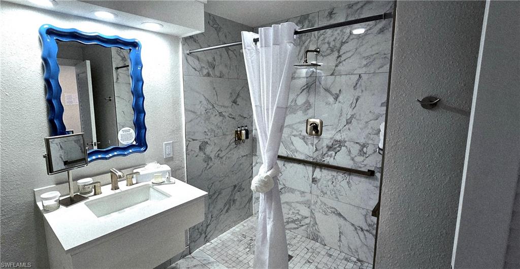 Bathroom with a textured wall, a marble finish shower, and vanity