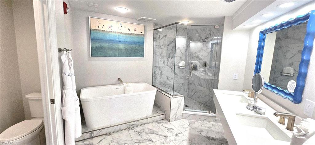 Full bath featuring double vanity, a freestanding bath, a marble finish shower, and light marble finish flooring