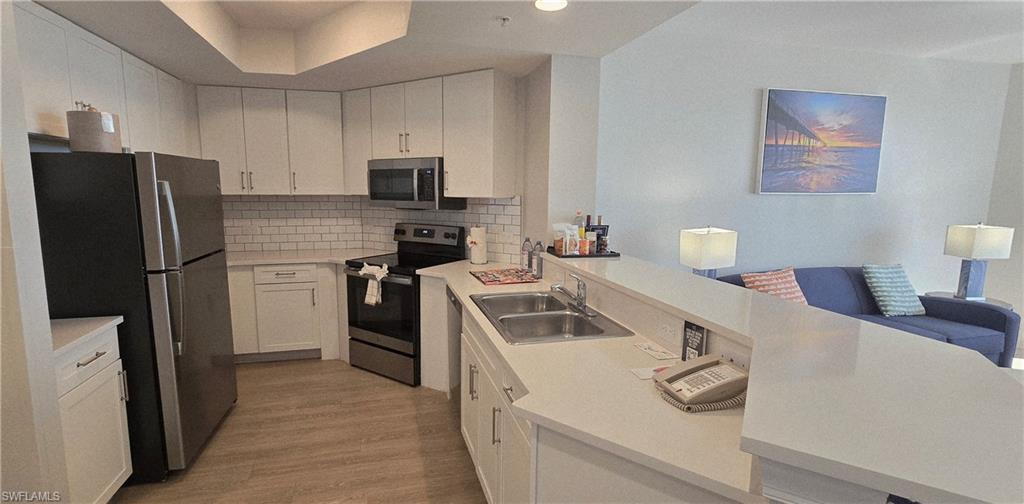 Kitchen featuring stainless steel appliances, white cabinetry, light countertops, decorative backsplash, and light wood-style floors