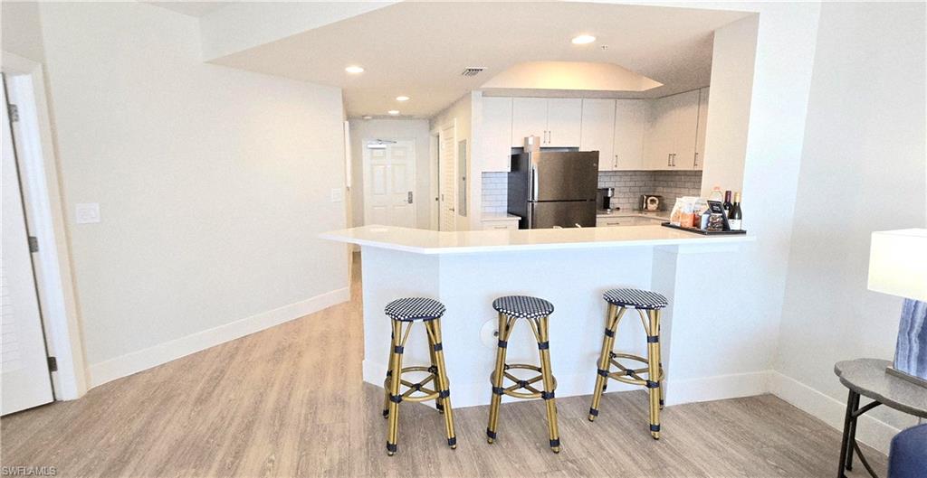 Kitchen with decorative backsplash, white cabinets, freestanding refrigerator, light wood-type flooring, and recessed lighting
