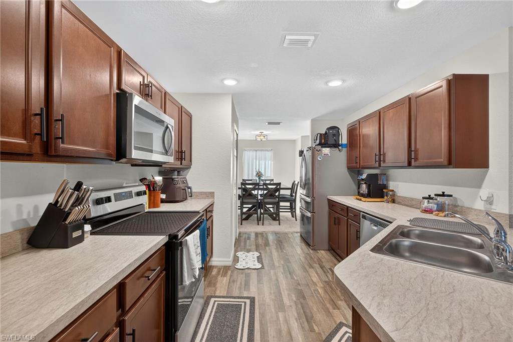 Kitchen featuring stainless steel appliances, light wood-type flooring, light countertops, brown cabinetry, and a textured ceiling