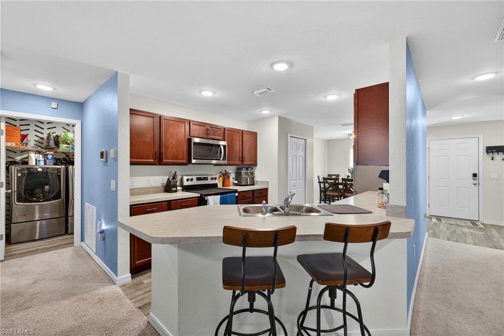 Kitchen featuring a kitchen bar, stainless steel appliances, light countertops, a peninsula, and brown cabinetry
