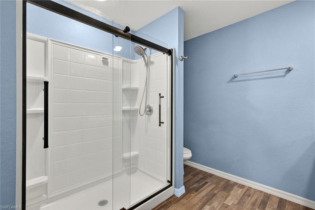 Full bathroom with dark wood finished floors, a stall shower, and a textured wall