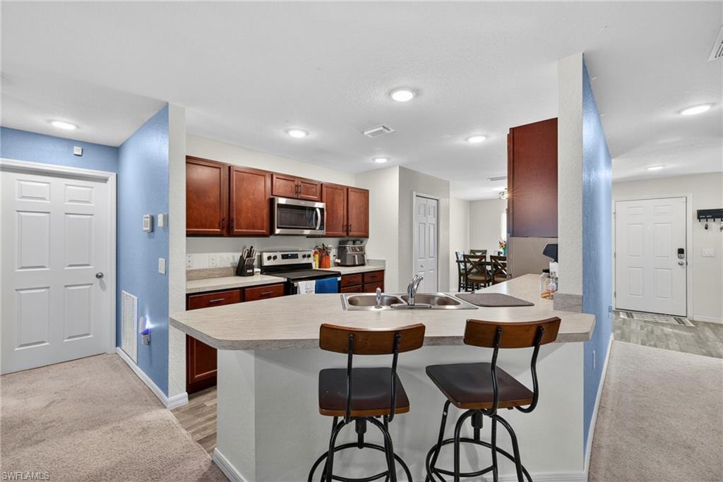 Kitchen with a kitchen breakfast bar, light carpet, stainless steel appliances, light countertops, and a peninsula