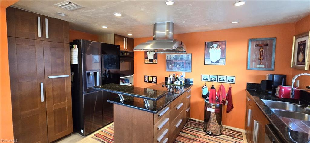 Kitchen featuring dark stone counters, black appliances, sink, a kitchen island, and island range hood