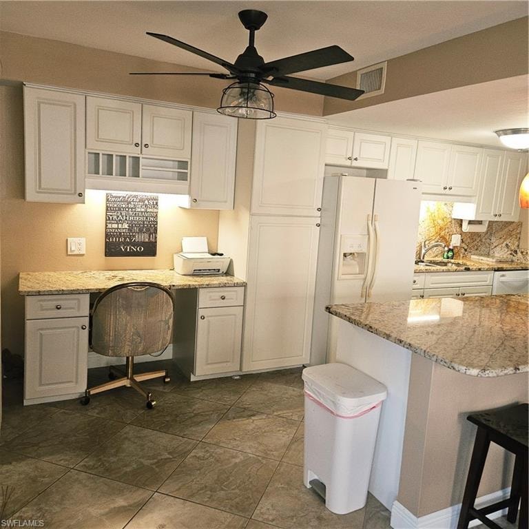 Kitchen featuring built in desk, light stone counters, refrigerator, white cabinetry, and decorative backsplash