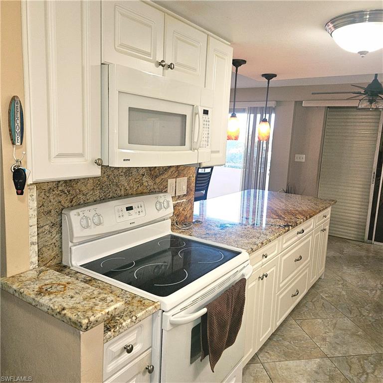 Kitchen with white appliances, light stone counters, decorative light fixtures, and white cabinets