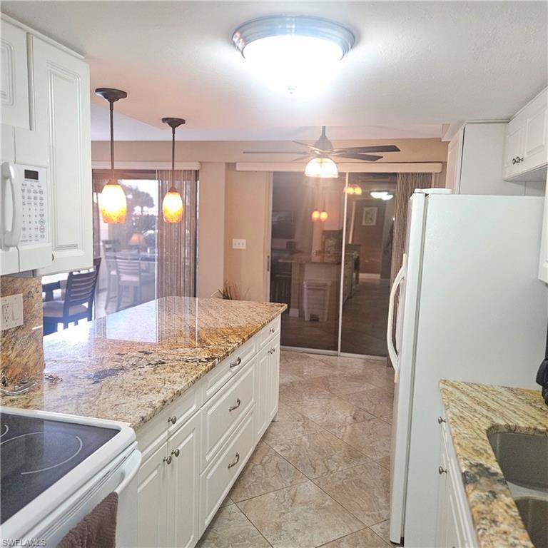 Kitchen with white cabinets, hanging light fixtures, white appliances, and light stone countertops