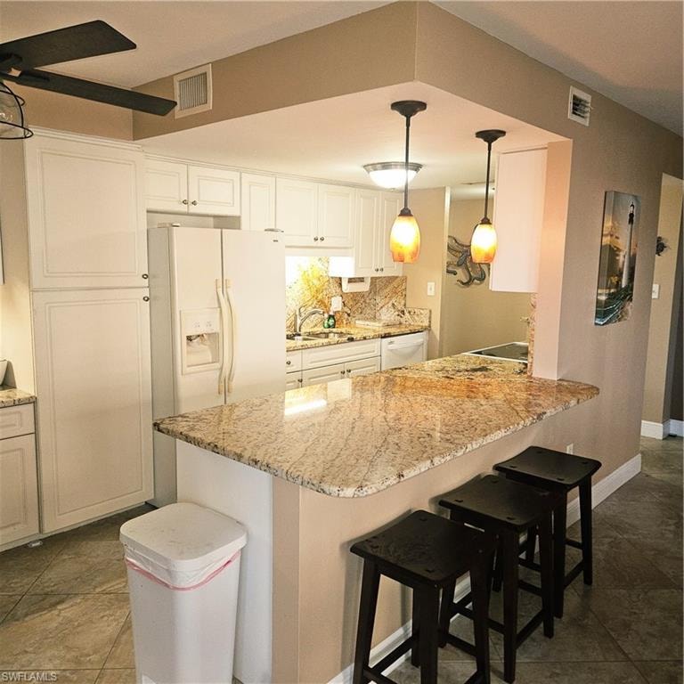 Kitchen with a kitchen bar, refrigerator, hanging light fixtures, a peninsula, and backsplash
