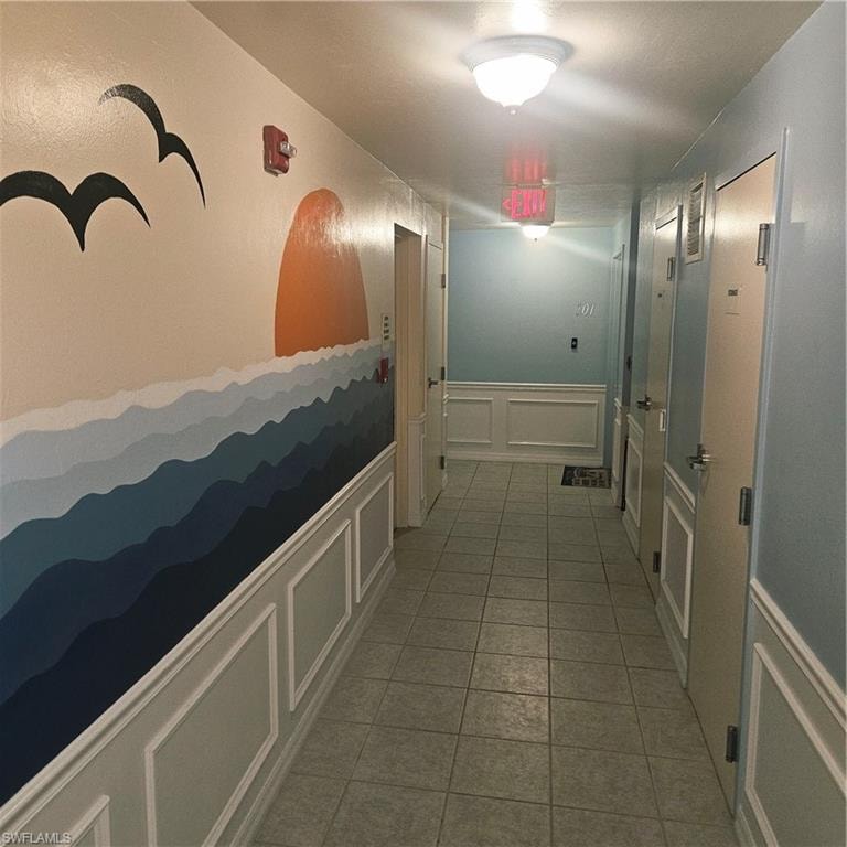 Corridor with a decorative wall, wainscoting, and light tile patterned floors
