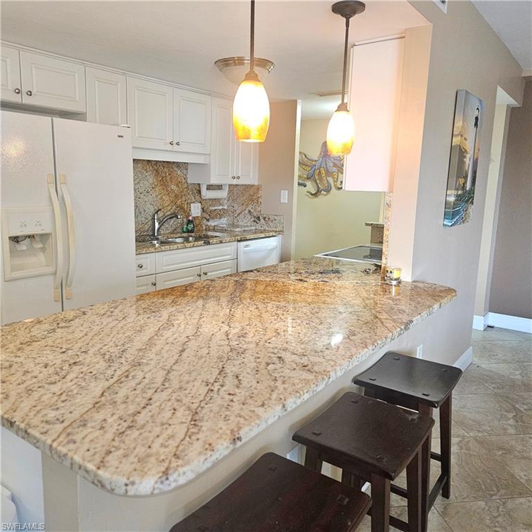 Kitchen featuring a breakfast bar area, white appliances, backsplash, light stone countertops, and a peninsula