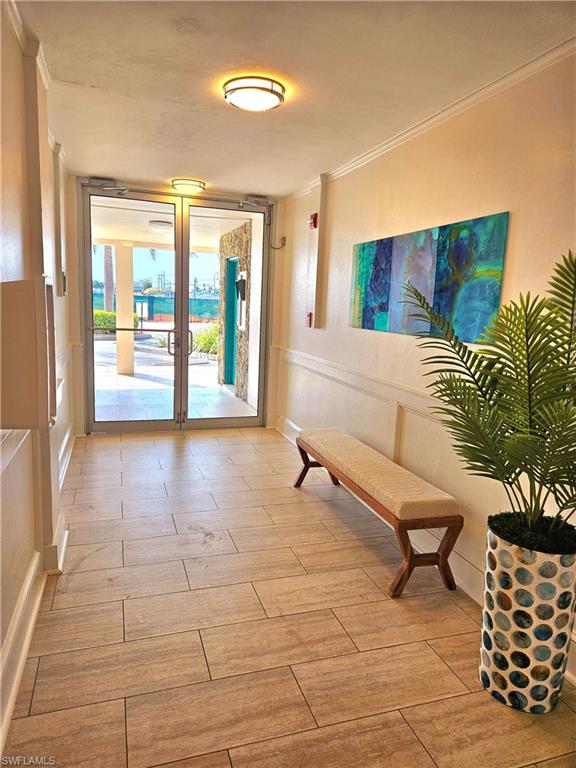 Doorway featuring crown molding, wood finish floors, and a wainscoted wall