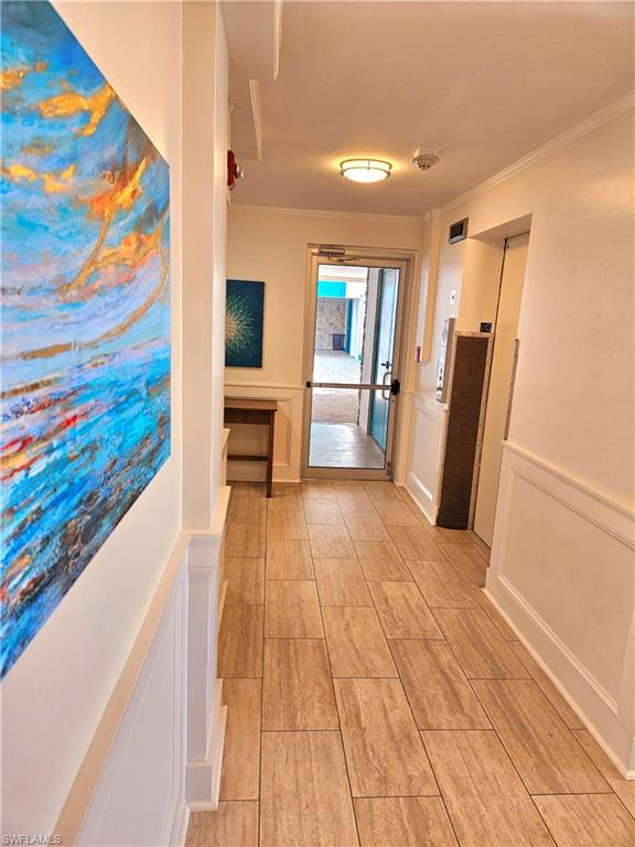 Corridor featuring a decorative wall, crown molding, and a wainscoted wall