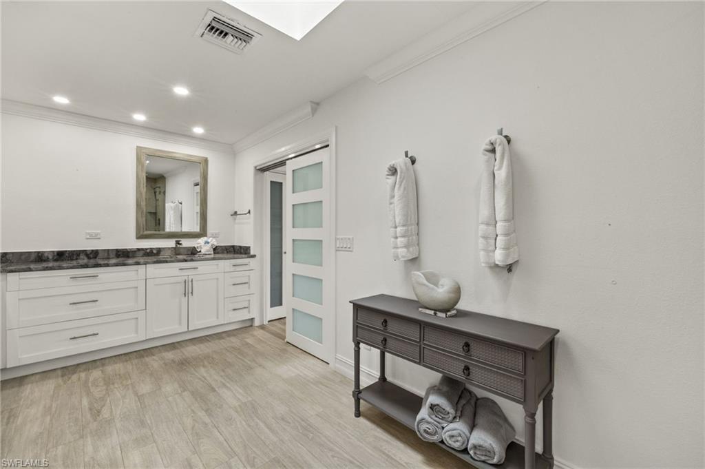 Full bath with vanity, ornamental molding, recessed lighting, light wood finished floors, and a skylight