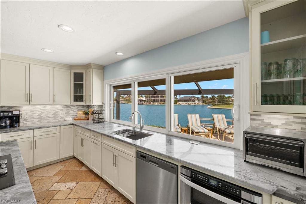 Kitchen with glass insert cabinets, decorative backsplash, light stone counters, and recessed lighting