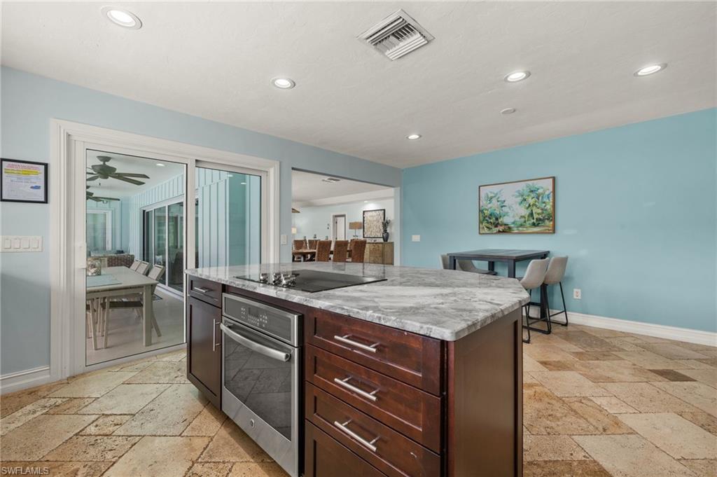 Kitchen with stainless steel oven, stone tile flooring, a kitchen island, recessed lighting, and light stone counters