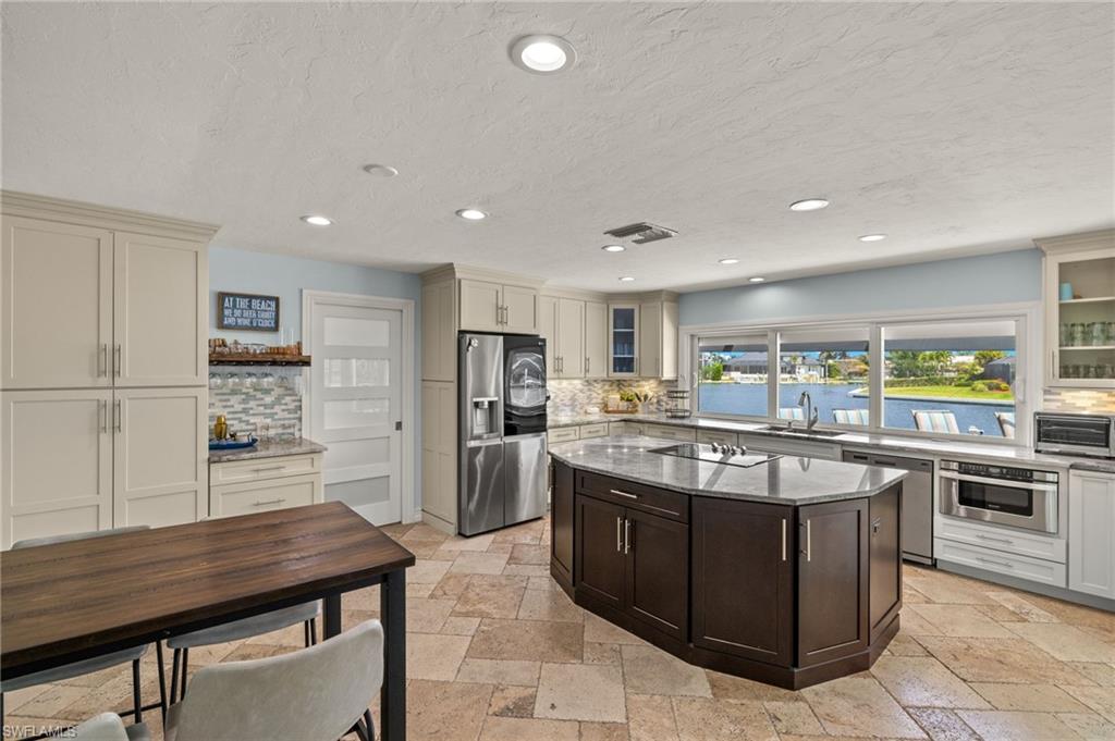Kitchen featuring glass insert cabinets, dark stone countertops, stainless steel appliances, recessed lighting, and stone tile flooring