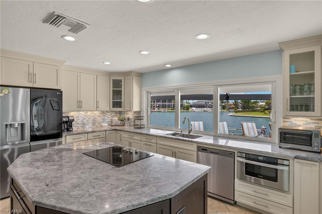 Kitchen with glass insert cabinets, decorative backsplash, light stone counters, appliances with stainless steel finishes, and recessed lighting