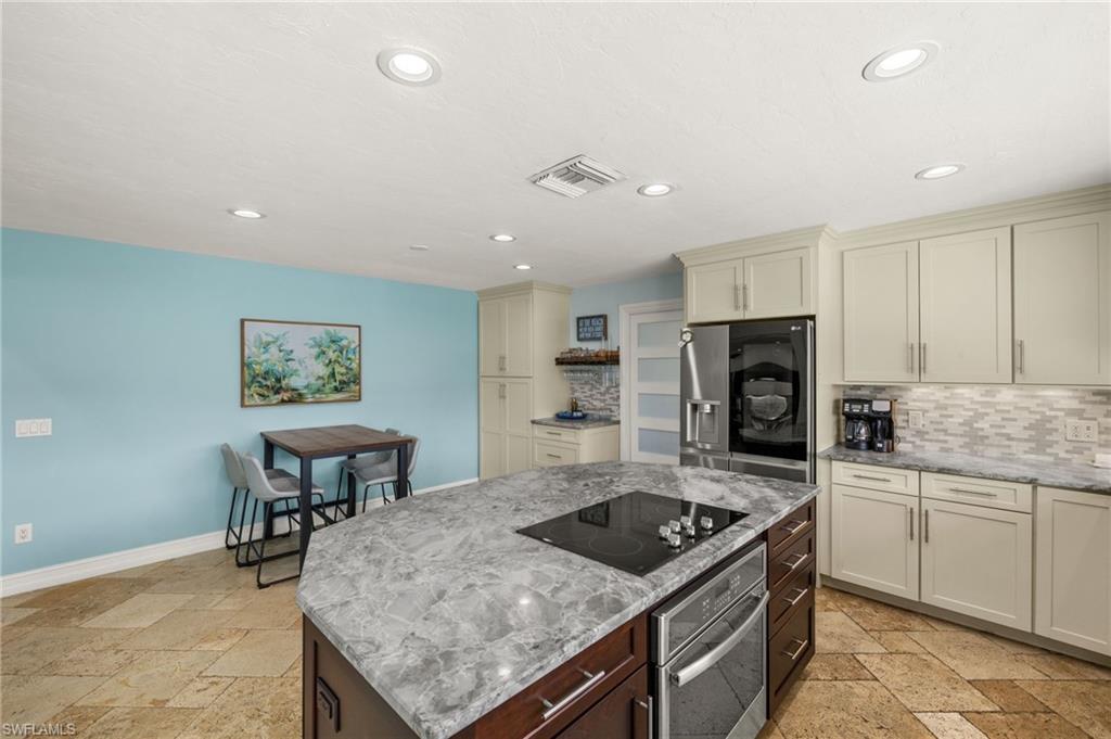 Kitchen featuring stone tile floors, light stone counters, cream cabinets, appliances with stainless steel finishes, and recessed lighting
