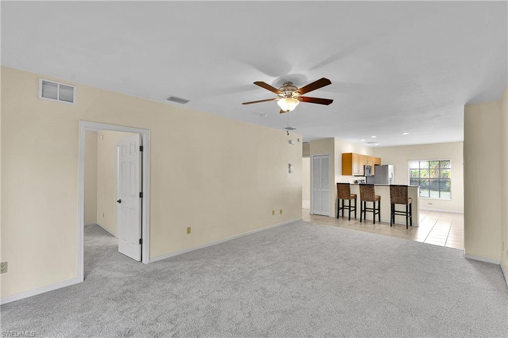 Living area with light carpet, a ceiling fan, and light tile patterned flooring