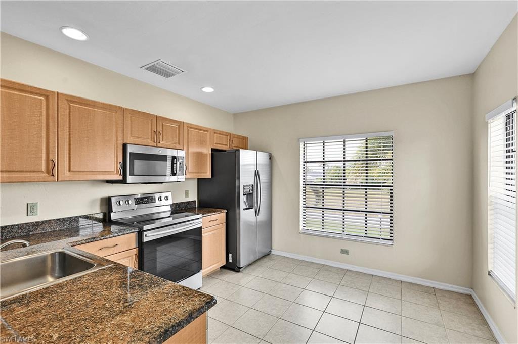Kitchen with stainless steel appliances, light tile patterned floors, recessed lighting, dark stone countertops, and brown cabinetry