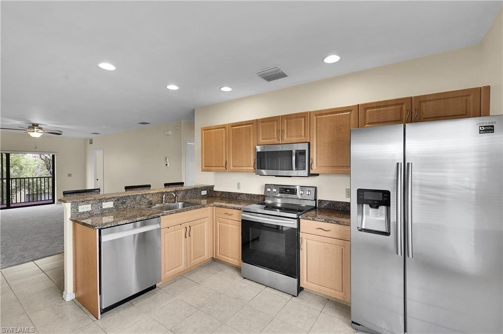 Kitchen with appliances with stainless steel finishes, recessed lighting, open floor plan, light tile patterned flooring, and dark stone counters