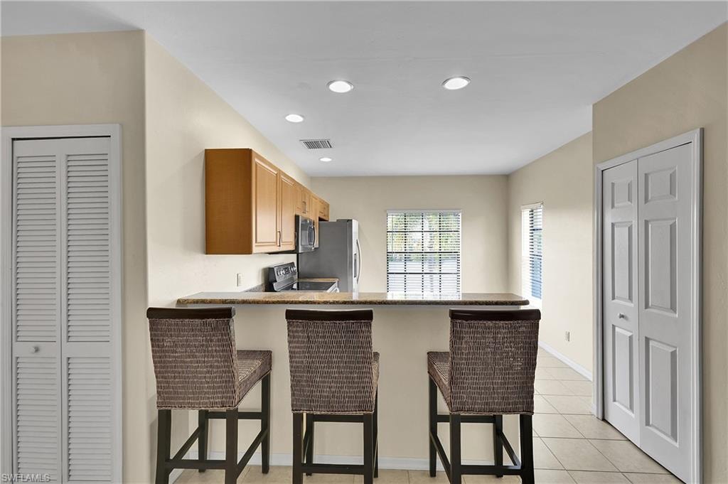 Kitchen with a kitchen bar, light tile patterned floors, a peninsula, stainless steel range with electric cooktop, and recessed lighting