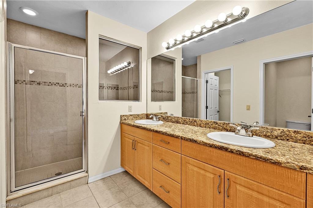 Full bathroom featuring light tile patterned floors, double vanity, a shower stall, and a walk in closet