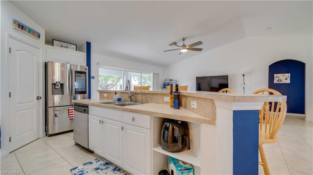 Kitchen featuring light tile patterned flooring, white cabinets, light countertops, stainless steel appliances, and lofted ceiling