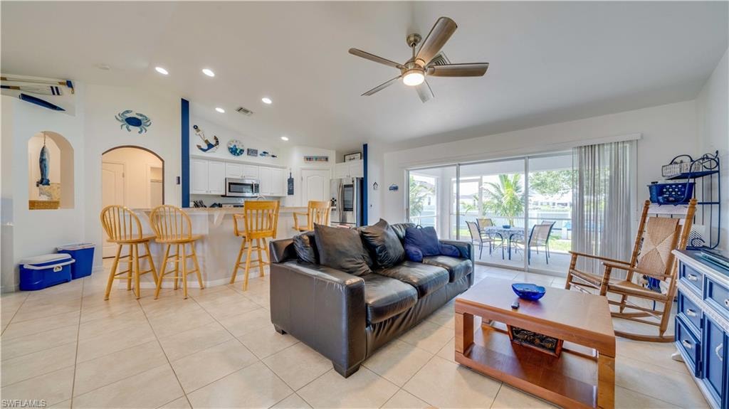Living area with vaulted ceiling, ceiling fan, light tile patterned floors, arched walkways, and recessed lighting