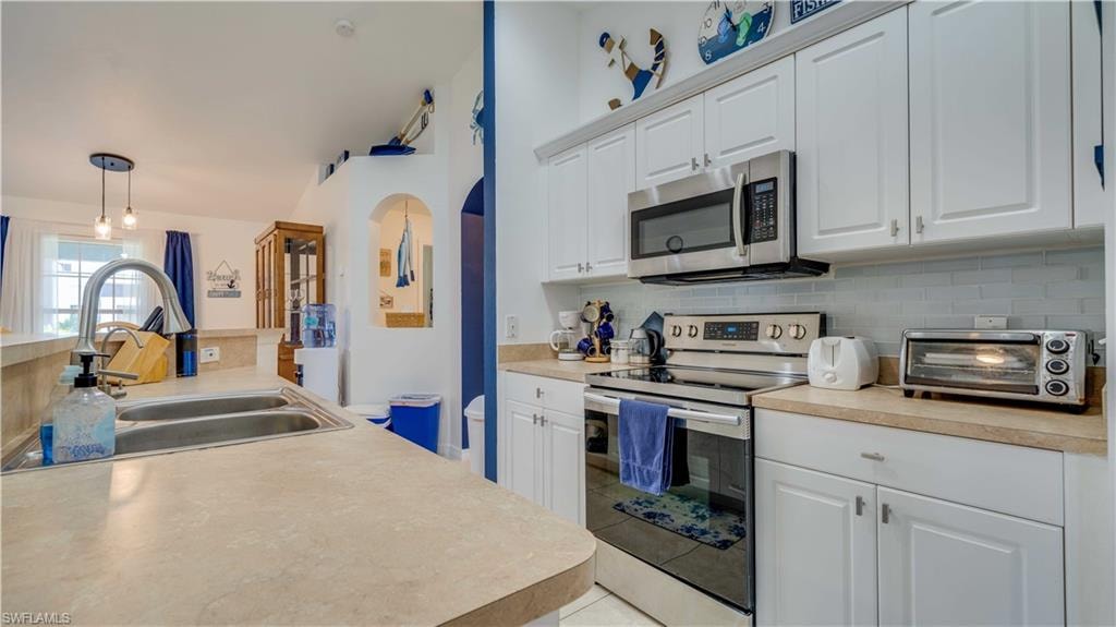 Kitchen with stainless steel appliances, white cabinetry, decorative backsplash, and light countertops