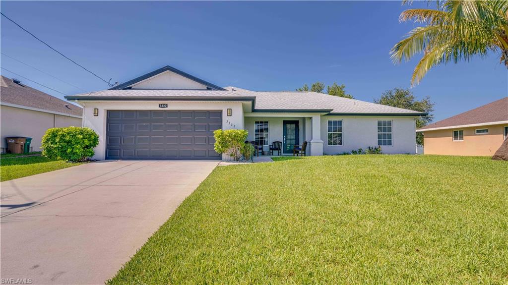 Single story home featuring stucco siding, a front yard, a garage, driveway, and covered porch
