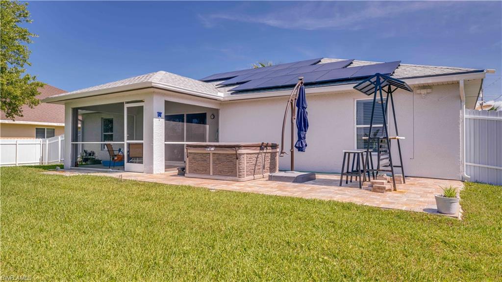 Back of house featuring a fenced backyard, stucco siding, solar panels, a hot tub, and a sunroom