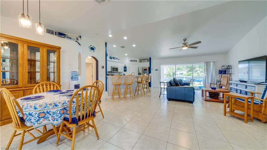 Dining space with vaulted ceiling, arched walkways, light tile patterned floors, recessed lighting, and ceiling fan